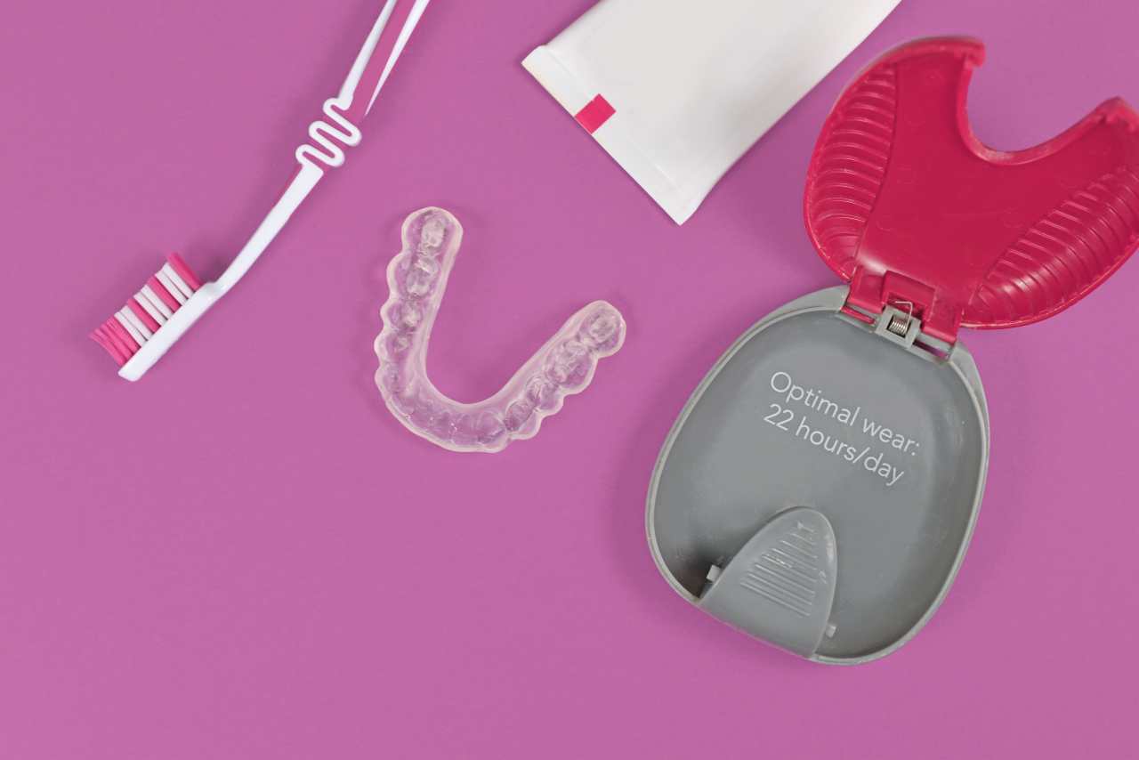 clear aligners for lower jaw with storing case, tooth brush and paste on pink background