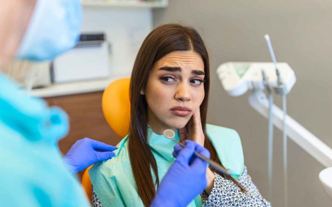 Young woman holding cheek in chair at dentist, having toothache. Shot of a young woman suffering from toothache while sitting in the dentist chair