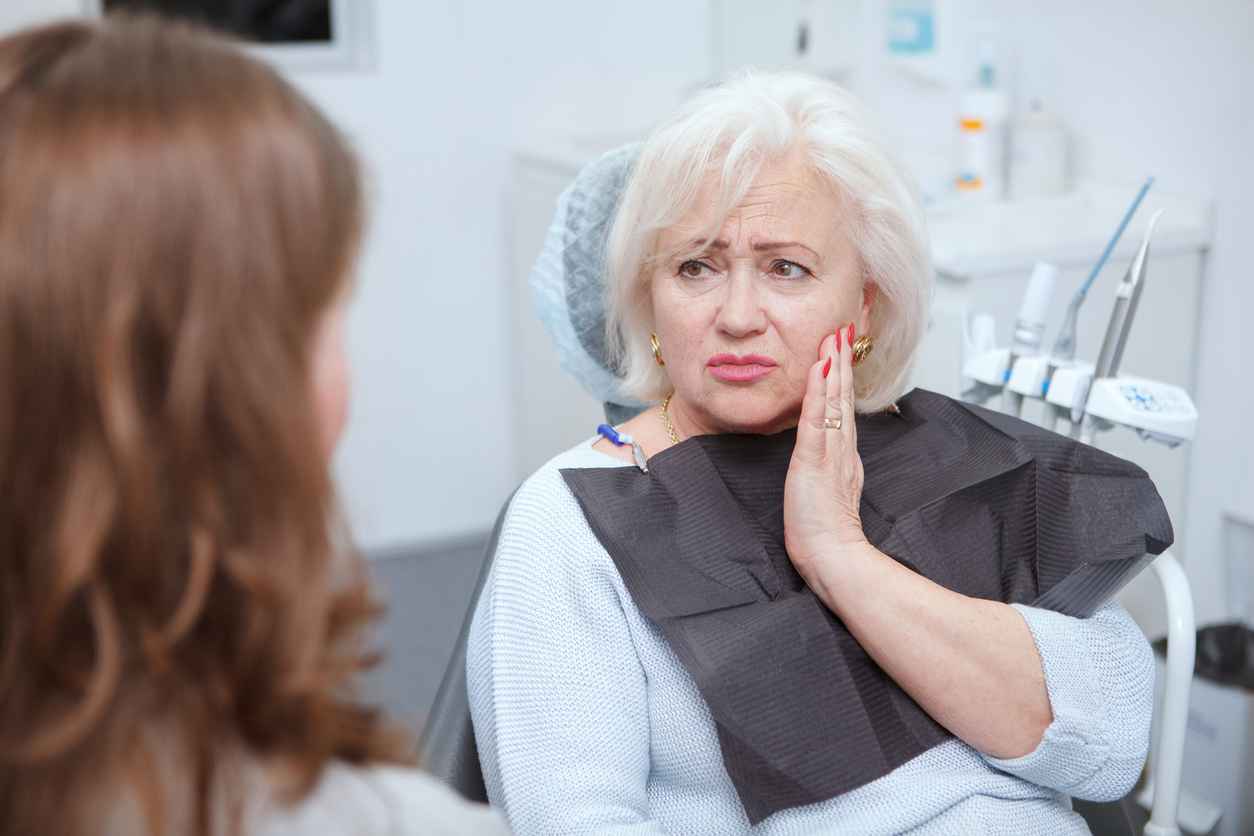 Elderly woman suffering from toothache, visiting dentist; Understanding Root Canals