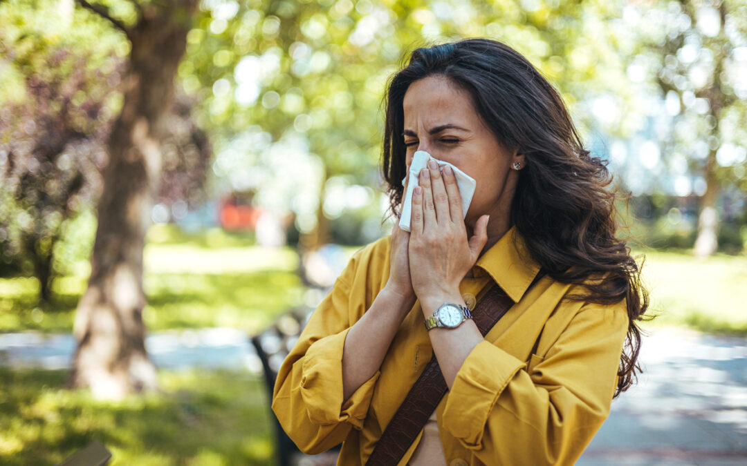 Portrait of unhealthy cute female in yellow top with napkin blowing nose